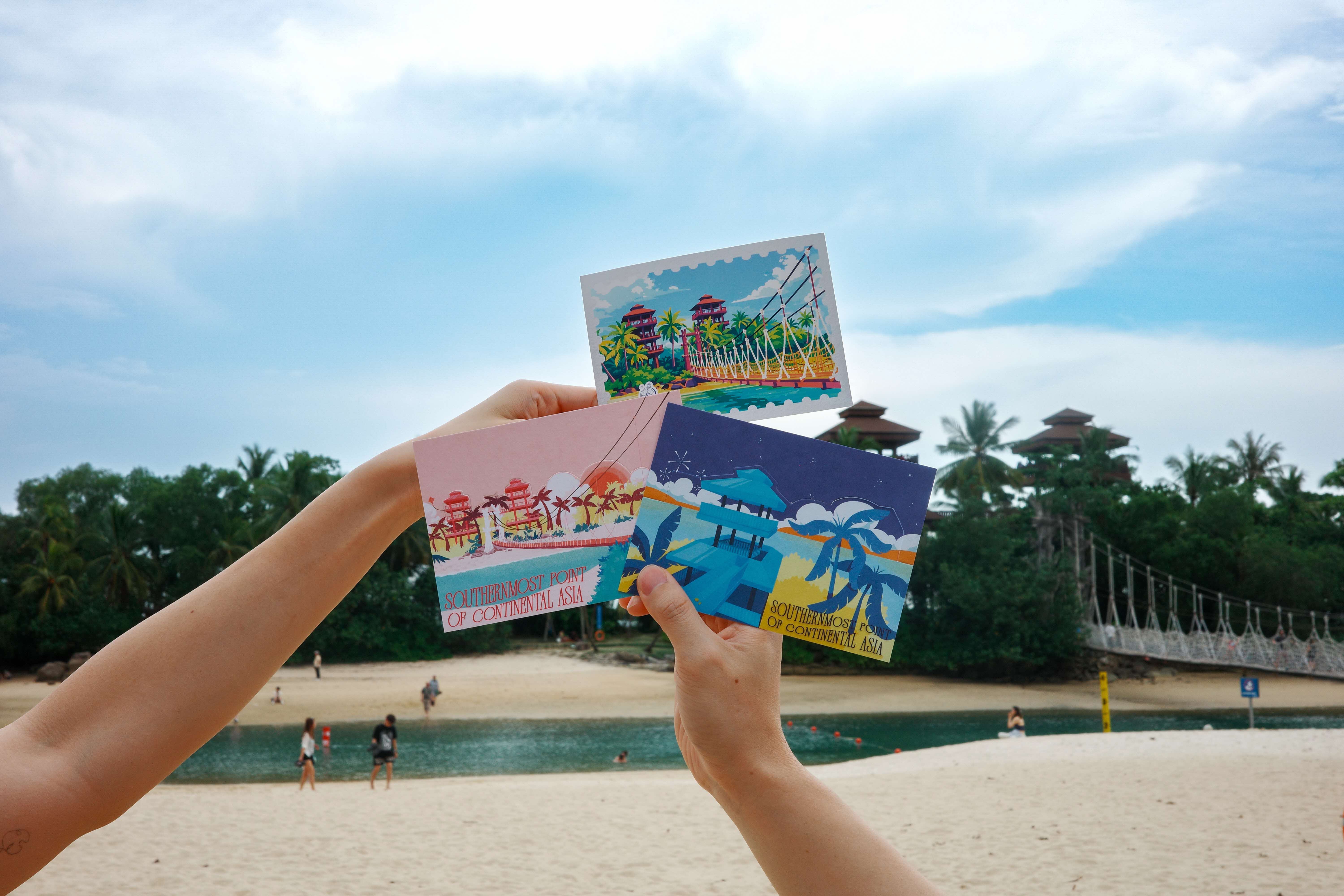 Threee postcard designs held up agains the beach